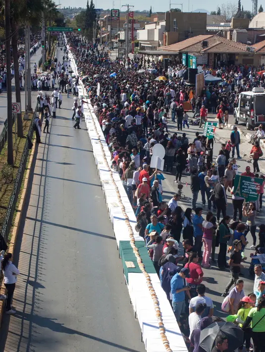 Orang-orang menyaksikan pembuatan kue raja sepanjang 2.063,43 meter di Saltillo, Negara Bagian Coahuila, Meksiko, 6 Januari 2019. Kue raja tersebut memecahkan Guinness World Record sebagai kue terpanjang di dunia. (Julio Cesar AGUILAR/AFP)