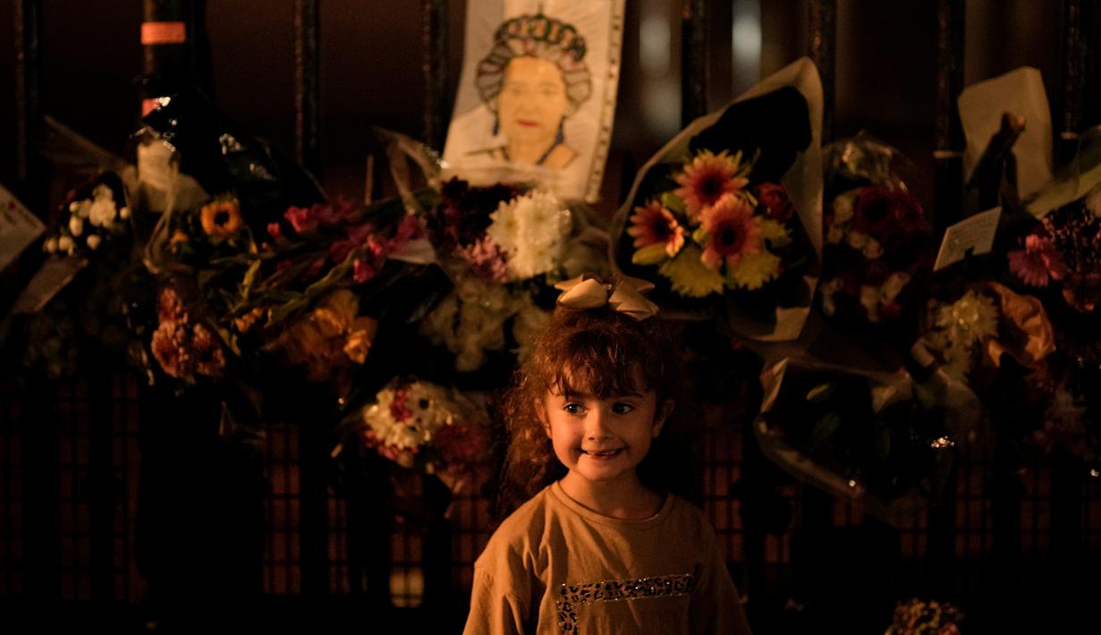 Seorang gadis kecil berpose didepan gambar Ratu Elizabeth II yang melekat pada pagar Istana Buckingham di London, Senin (12/9/2022). Pada usia 19 tahun, dia dilaporkan bergabung dengan Women's Auxiliary Territorial Service untuk dilatih sebagai supir dan mekanik. (AP Photo/Vadim Ghirda)