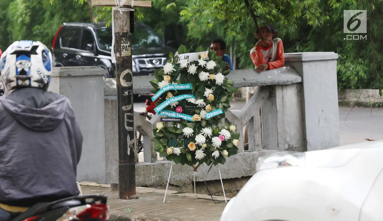 Warga berdiri dekat karangan bunga yang bersandar pada tiang lampu yang ditabrak mobil yang ditumpangi Ketua DPR Setya Novanto di Jalan Permata Berlian, Jakarta, Sabtu (18/11). Dalam karangan bunga tersebut tertulis pesan. (Liputan6.com/Angga Yuniar)