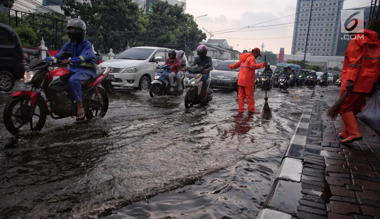 Petugas dari Dinas Kebersihan membuang genangan air kedalam selokan usai hujan deras dikawasan Tugu Tani, Jakarta, Kamis (12/10). Tingginya curah hujan membuat genangan disisi jalan. (Liputan6.com/Faizal Fanani)