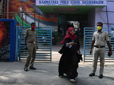 Polisi berjaga-jaga ketika seorang siswa sekolah menengah negeri dan perguruan tinggi pra-universitas untuk wanita melangkah keluar untuk mengembalikan telepon kepada orang tuanya yang berdiri di luar tempat institut pendidikan di Bangalore (16/2/2022). (AFP/Manjunath Kiran)