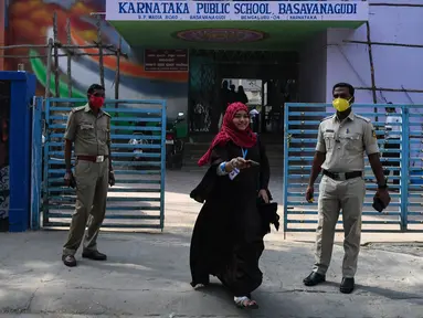 Polisi berjaga-jaga ketika seorang siswa sekolah menengah negeri dan perguruan tinggi pra-universitas untuk wanita melangkah keluar untuk mengembalikan telepon kepada orang tuanya yang berdiri di luar tempat institut pendidikan di Bangalore (16/2/2022). (AFP/Manjunath Kiran)