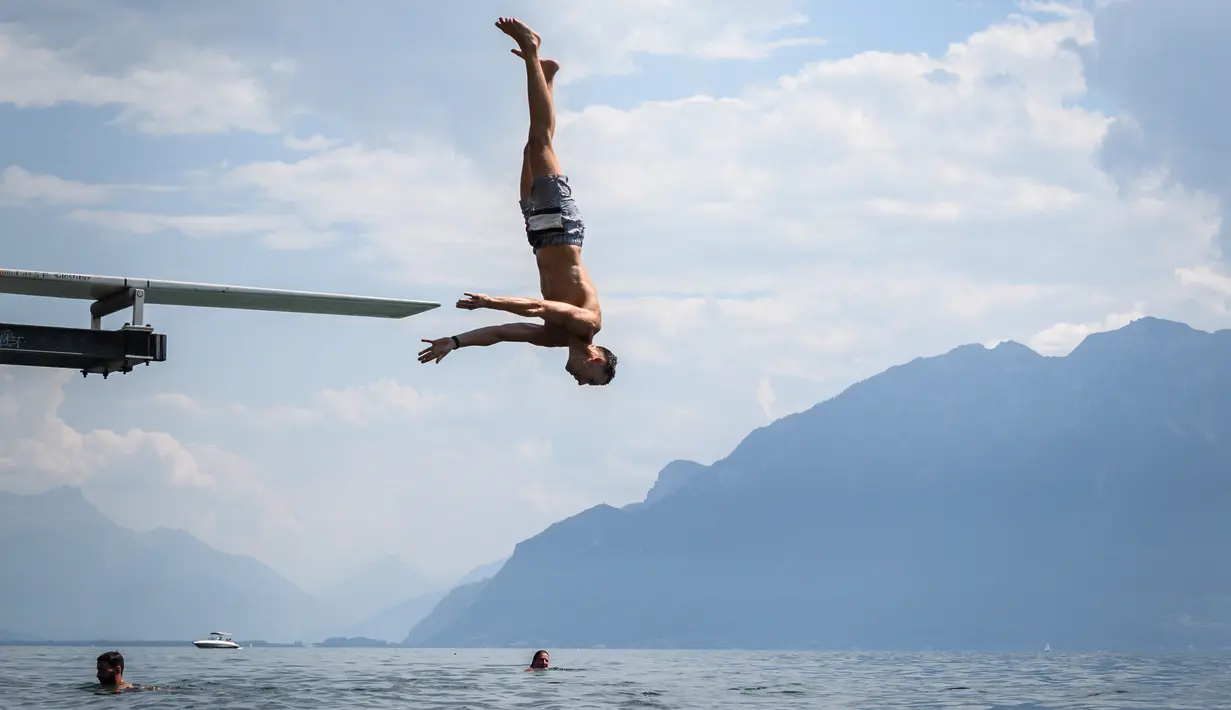 Seorang pria melompat ke Danau Jenewa di Saint Saphorin, Swiss barat saat gelombang panas melanda seluruh Eropa utara (31/7). Kondisi kekeringan di sebagian daerah diperkirakan akan terus berlanjut. (AFP Photo/Fabrice Coffrini)