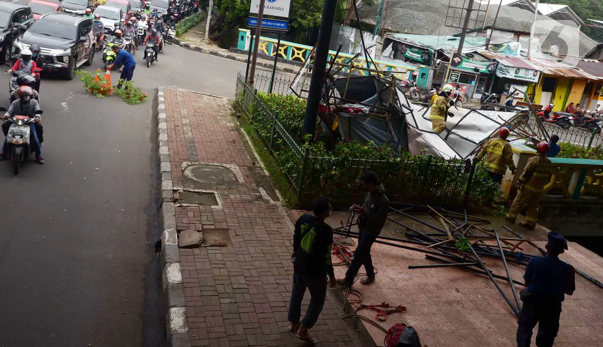 Kondisi lalu lintas saat petugas pemadam kebakaran memotong rangka reklame yang roboh di Jalan Soepomo, Jakarta, Sabtu (28/5/2022). Hujan disertai angin kencang pada pagi tadi membuat papan reklame roboh sehingga membuat kemacetan arus lalu lintas di jalan tersebut. (merdeka.com/Imam Buhori)