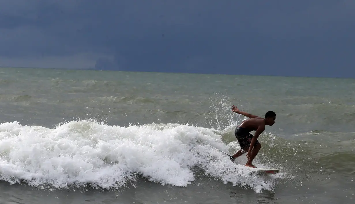 Abu Dzar Al-Ghifari berselancar ketika Gunung Krakatau (kiri) dan Anak Krakatau terlihat di lepas pantai Carita, Banten (26/12). Pemerintah meminta warga menghindari pantai di daerah-daerah tersebut. (AP Photo/Achmad Ibrahim)