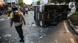 Polisi berjalan dekat sebuah mobil polisi yang dirusak massa saat bentrok di kawasan Pejompongan, Jakarta, Rabu (7/10/2020). (Liputan6.com/Faizal Fanani)