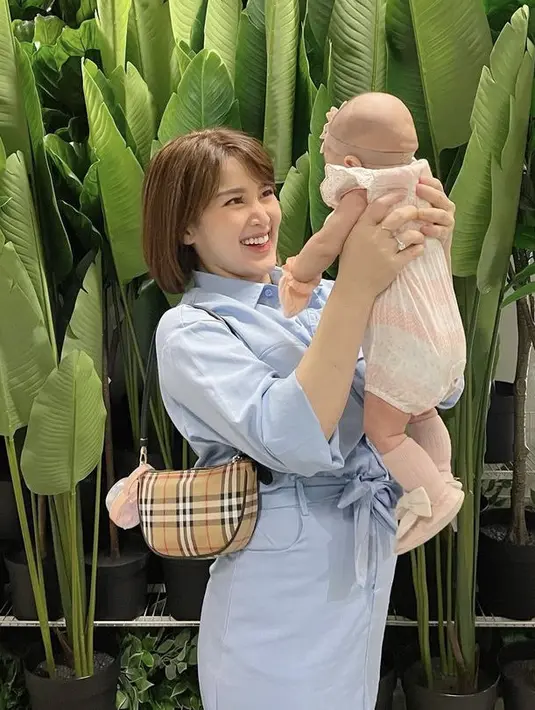 <p>Menggedong sang anak, ia pun tampil layaknya mama muda dengan kemeja dan skirt warna baby blue. Tak lupa membawa slingbagnya.&nbsp;@rsn.dw</p>