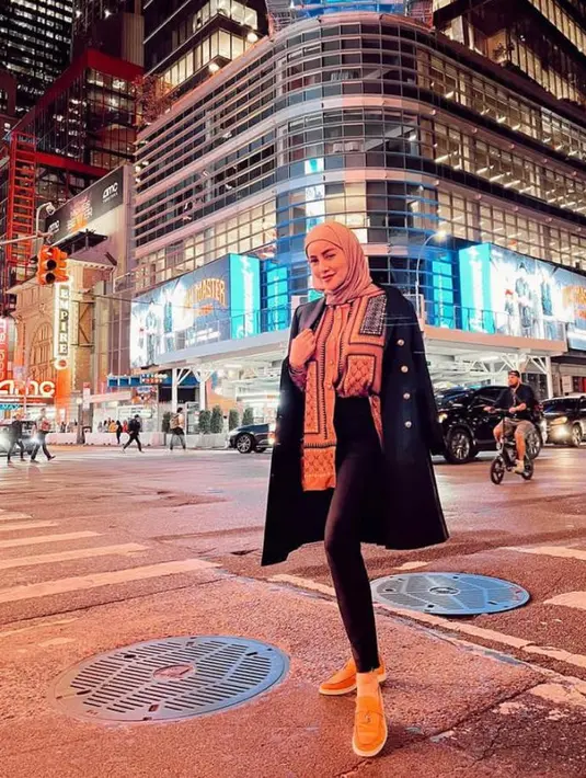 Olla tampak mengenakan blouse bermotif yang dilapisi long coat hitam, hijab dan celana panjang senad