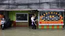 Dengan ketinggian air bervariasi, banjir rob di kawasan Muara Baru Jakarta juga merendam akses jalan utama. Tampak dalam foto, seorang pria menggendong anak membeli makanan siap saji di sebuah rumah makan saat jalanan terendam banjir akibat pasang tinggi di Muara Baru, Jakarta, pada Sabtu 6 Desember 2025. (ADITYA IRAWAN/AFP)