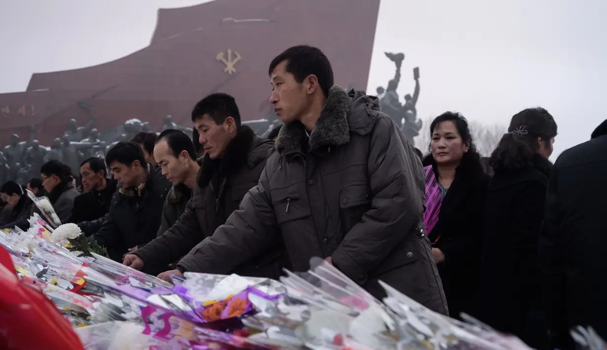 Penduduk Pyongyang meletakkan bunga di depan patung pemimpin Korea Utara Kim Il Sung dan Kim Jong Il selama Hari Peringatan Nasional di Bukit Mansu, Pyongyang (17/12).  Korea Utara tengah memperingati 7 tahun wafatnya  Kim Jong Il. (AFP Photo/Kim Won Jin)