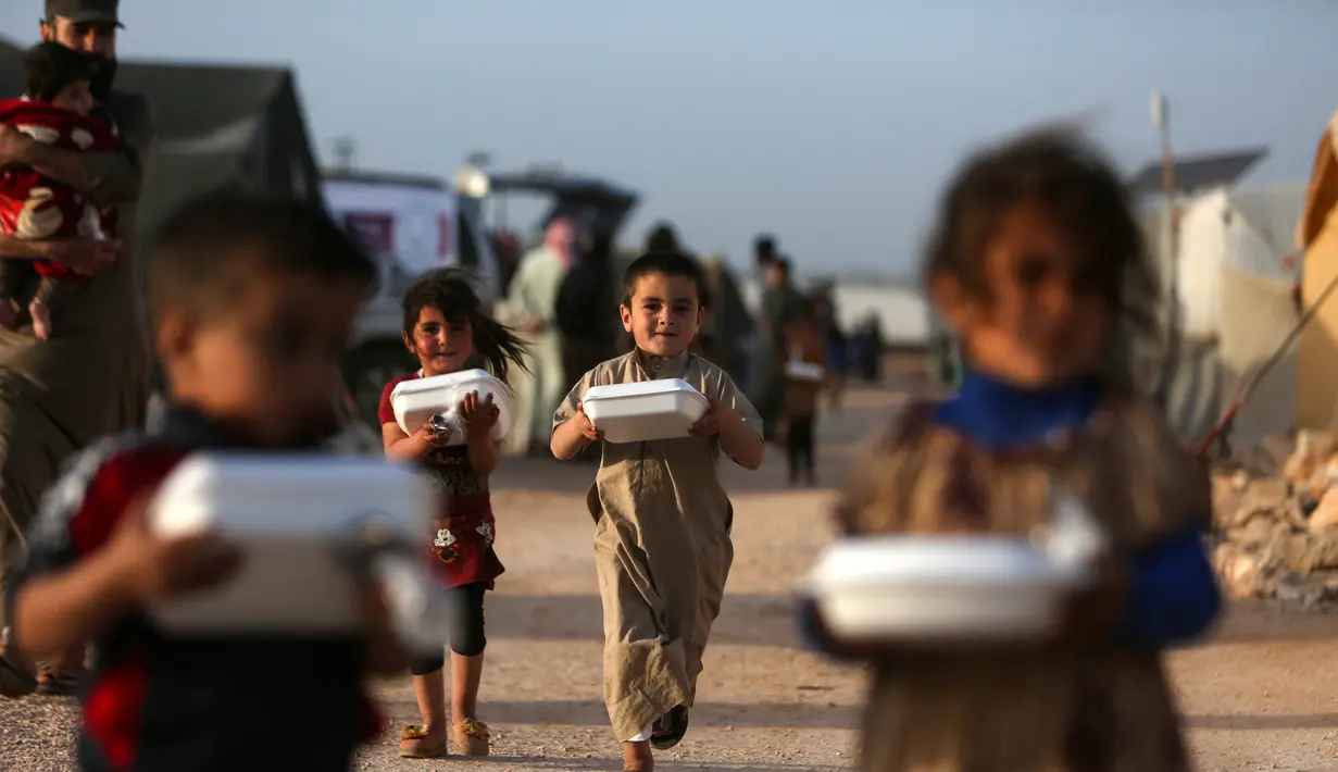 Anak-anak Suriah kembali ke tenda mereka dengan kotak-kotak makanan yang didistribusikan organisasi amal lokal, sebelum berbuka puasa selama bulan suci Ramadhan di kamp pengungsi di pinggiran kota Dana yang dikuasai pemberontak, timur perbatasan Turki-Suriah di Idlib (3/4/2022). (AFP/Aaref Watad)