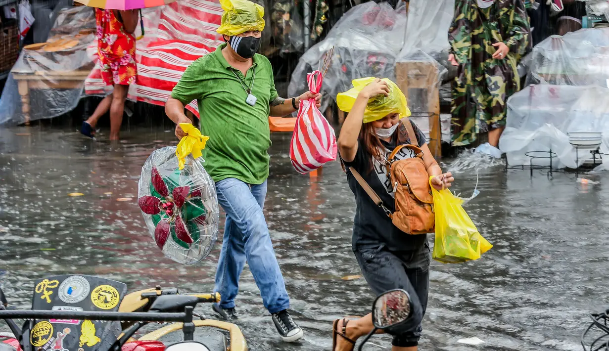 Orang-orang berjalan melewati banjir di tengah hujan deras yang tiba-tiba mengguyur di sebuah pasar dekorasi Natal di Manila, Filipina (9/12/2020). (Xinhua/Rouelle Umali)