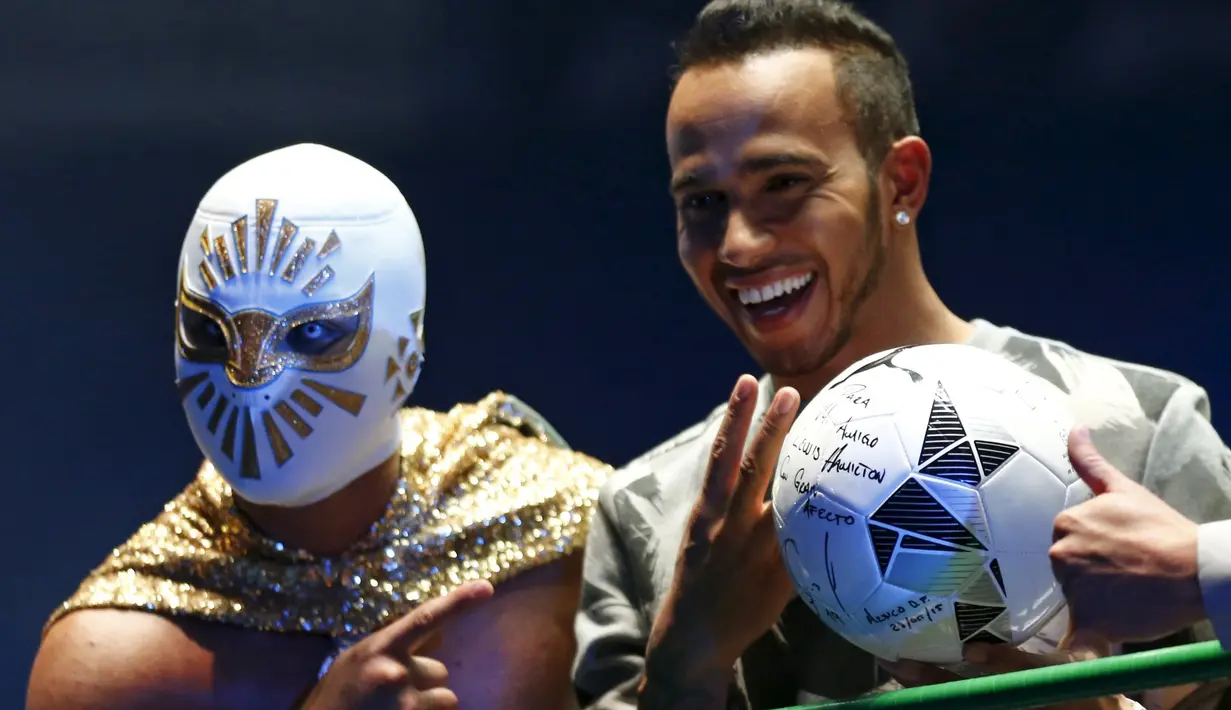 Pebalap F1 dari tim Mercedes GP, Lewis Hamilton dengan bola yang ditandatanganinya bersama seorang bintang WWE dalam sebuah acara promosi di Coliseo Arena, Mexico City, (28/10/2015). (Reuters/Henry Romero)