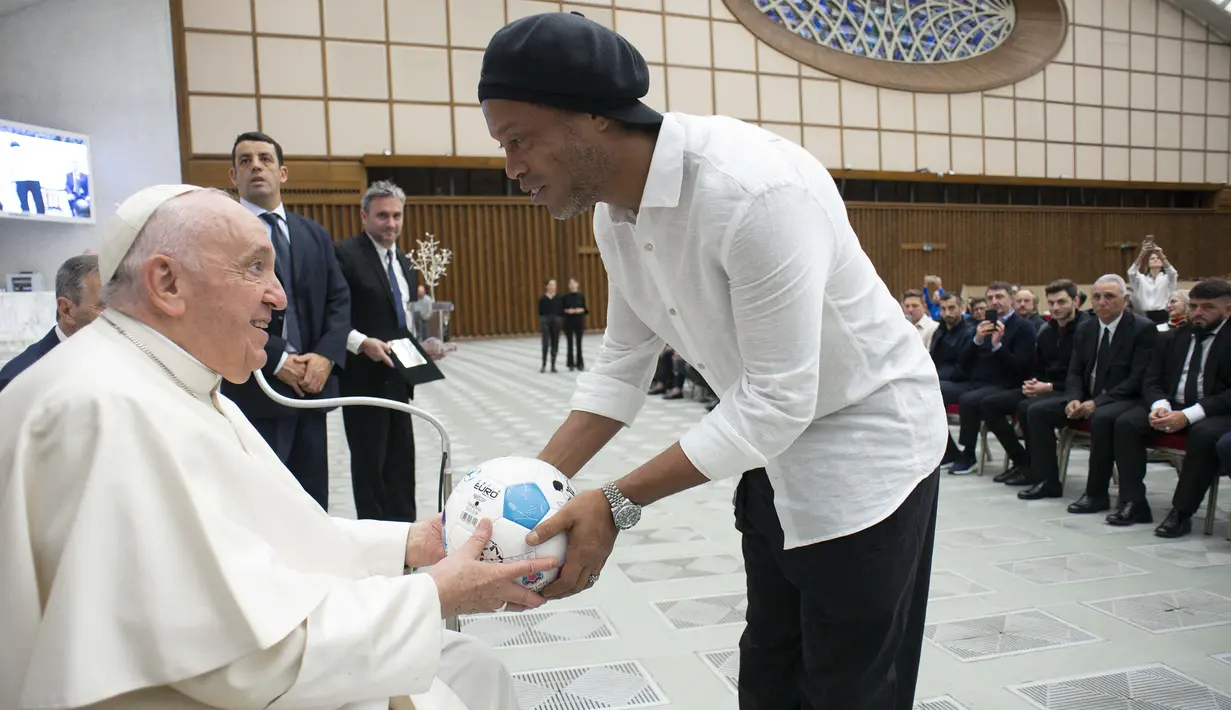 Mantan pesepak bola Brasil, Ronaldinho memberikan bola kepada Paus Fransiskus saat menghadiri audiensi dengan peserta pertandingan penghormatan "match for peace" untuk mengenang mendiang pemain Argentina, Diego Maradona, pada 14 November 2022 di aula Paul-VI, Vatikan. Pertandingan ini diselenggarakan oleh "WePlayForPeace", sebuah yayasan yang didirikan oleh Paus Fransiskus. (AFP/Vatican Media)