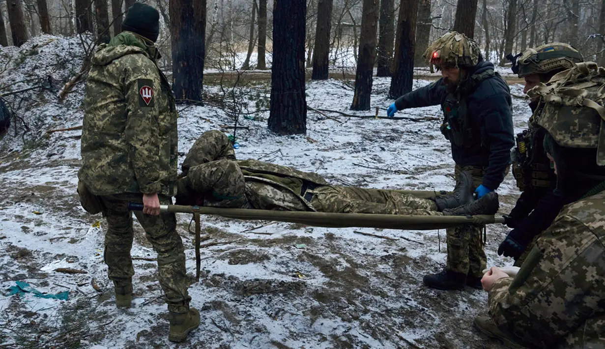 Petugas medis militer membawa tentara yang terluka ke kendaraan evakuasi dekat Kremenna di wilayah Luhansk, Ukraina, 16 Januari 2023. Hingga saat ini pejabat Ukraina menolak untuk mengonfirmasi jumlah korban dalam perangnya dengan Rusia, setelah ketua Komisi Uni Eropa pada akhir November 2022 lalu memperkirakan bahwa "lebih dari 20.000 warga sipil dan 100.000 tentara Ukraina telah tewas di Ukraina hingga saat ini." (AP Photo/LIBKOS)