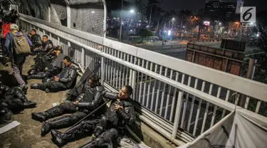 Aparat kepolisan melepas lelah di jembatan penyeberangan orang (JPO) depan Gedung DPR, Jakarta, Selasa (24/9/2019). Mereka melepas lelah usai mengawal demonstrasi mahasiswa menolak pengesahan RUU KUHP dan revisi UU KPK. (Liputan6.com/Faizal Fanani)