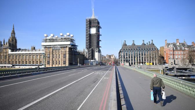 Sebuah gambar menunjukkan Gedung Parlemen (kiri) di ujung Westminster Bridge yang kosong dengan seorang pejalan kaki di trotoar London setelah pemerintah Inggris setempat memberlakukan lockdown akibat pandemi Covid-19 pada 24 Maret 2020. (Photo by JUSTIN TALLIS / AFP)