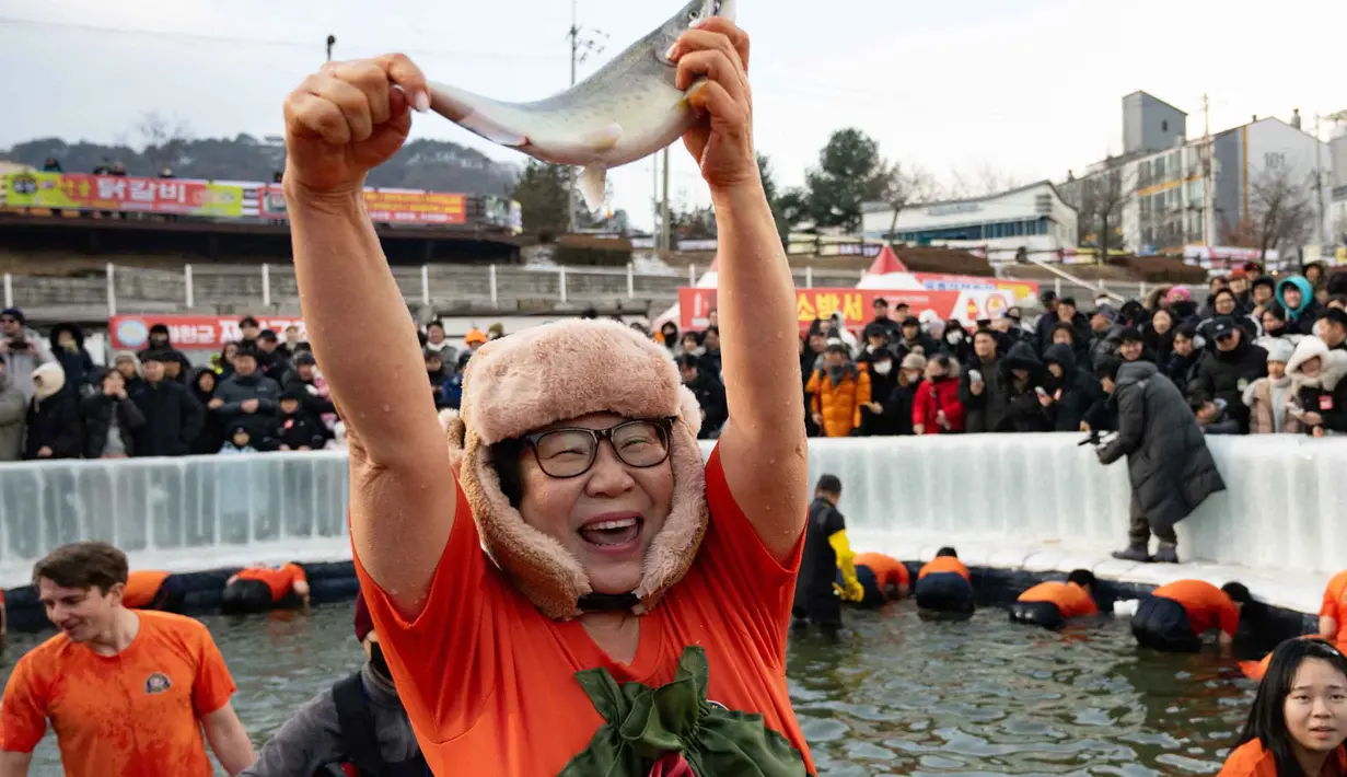 Penyelenggara memperkirakan festival ini akan menarik lebih dari satu juta pengunjung tahun ini, termasuk target 100.000 wisatawan mancanegara. Tampak dalam foto, seorang wanita bereaksi saat menangkap ikan trout dengan tangan selama festival tahunan memancing di atas es, Hwacheon, Korea Selatan, pada Sabtu 10 Januari 2026. (Shin Yong-ju/AFP)