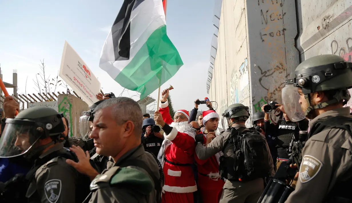 Pengunjuk rasa berkostum sinterklas (Santa Claus) berhadapan dengan polisi perbatasan Israel dalam demonstrasi di Bethlehem, Tepi Barat, 23 Desember 2017. Protes terkait pengakuan Donald Trump atas Yerusalem sebagai Ibu Kota Israel. (AP/Nasser Shiyoukhi)