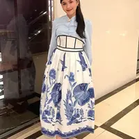 Erina Gudono tampil mengenakan rok high waist warna putih dengan aksen batik ikan floral waena biru. Dipadukan dengan kemeja lengan panjang baby blue dan bros di bagian kerah. Ia pun memadukan dengan sandal Hermes warna coklat. [@erinagudono]