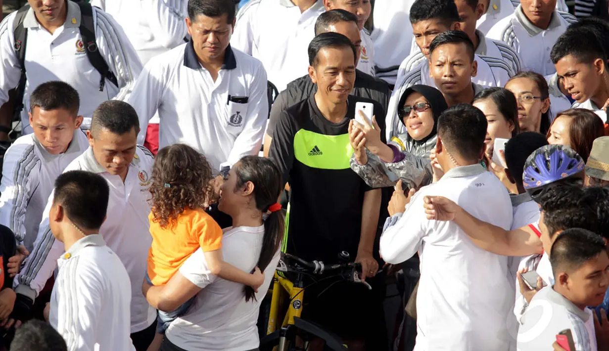 Presiden RI, Joko Widodo bersepeda di Hari Bebas Kendaraan Bermotor di kawasan Bundaran Hotel Indonesia, Minggu (11/1/2015). Tampak salah satu warga berfoto bersama Presiden Jokowi. (Liputan6.com/Faizal Fanani)