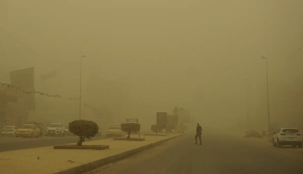<p>Seorang pria menyeberang jalan selama badai pasir Musim Semi di ibukota Irak, Baghdad (5/5/2022). Irak dihantam oleh serangkaian badai semacam itu pada bulan April, menghentikan penerbangan dan membuat puluhan orang dirawat di rumah sakit karena masalah pernapasan. (AFP/Sabah Arar)</p>