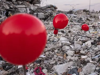 Balon yang tergantung di puing-puing bangunan yang runtuh di Antakya, Turki selatan, menyusul gempa berkekuatan 6,4 yang melanda pada 20 Februari, dua minggu setelah gempa berkekuatan 7,8 melanda dekat Gaziantep dan telah menewaskan lebih dari 44.000 orang.  Di sisi jalan yang sibuk di Antakya, puluhan balon merah berkibar, bergelantungan di reruntuhan.  (AFP/Sameer Al-Doumy)