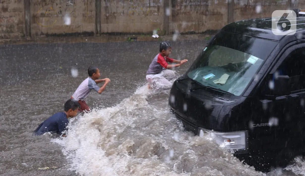 Sejumlah anak bermain banjir saat melanda jalan Bayangkara Pusdiklat, Kota Tangerang Selatan, Banten, Selasa (2/11/2021). Aksi anak anak tersebut dapat membahayakan keselamatan jiwa karena banyaknya kendaraan yang melintas menerjang banjir. (Liputan6.com/Angga Yuniar)