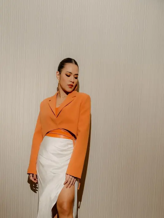 <p>Dalam foto kali ini, Raisa tampil manggung mengenakan cropped blazer bernuansa oranye, dipadu dengan white satin midi skirt yang juga memiliki high slit. Ia tambahkan belt bernuansa oranye yang senada dengan blazernya sebagai statement yang menarik. Foto: Instagram.</p>