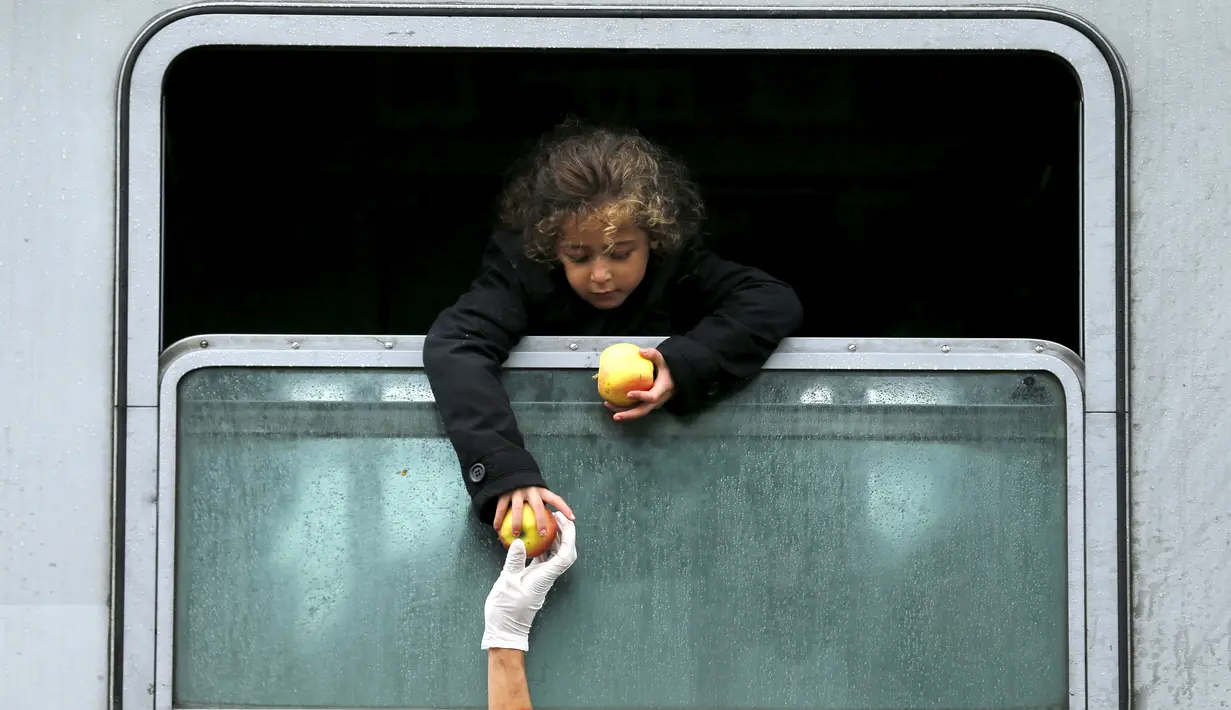 Seorang anak imigran bersandar keluar dari jendela kereta untuk mengambil makanan di stasiun kereta api Tovarnik, Kroasia, 29 September 2015. (REUTERS/Antonio Bronic)