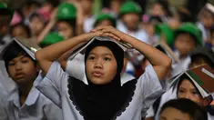 Para pelajar muda meletakkan buku di kepala mereka saat berkumpul di pusat evakuasi yang telah ditentukan di luar gedung sekolah selama latihan gempa bumi di salah satu sekolah dasar di Manila, Filipina pada 11 September 2025. (Ted ALJIBE/AFP)