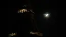 Bulan terlihat di sebelah Menara Eiffel yang lampunya dimatikan di Paris, Rabu (21/10/2020). Kondisi gelap gulita itu untuk memberikan penghormatan terhadap Samuel Paty, seorang guru sejarah yang dipenggal kepalanya pada Jumat (16/10) lalu. (GEOFFROY VAN DER HASSELT / AFP)