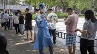 Seorang pekerja yang mengenakan pakaian pelindung dan membawa megafon memegang selembar dengan kode QR untuk orang-orang yang mengantre untuk tes virus corona COVID-19 di tempat pengujian pada hari ketiga pengujian massal untuk jutaan penduduk di Distrik Chaoyang, Beijing, China, 15 Juni 2022. (AP Photo/Mark Schiefelbein)