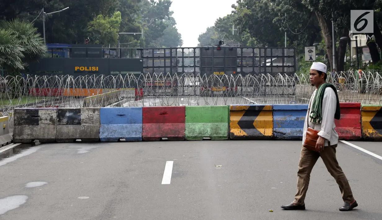 Salah satu peserta aksi berjalan di depan barikade penutup sebagian Jalan Medan Merdeka Barat, Jakarta, Jumat (14/6/2019). Massa berkumpul menyampaikan pendapat terkait sidang perselisihan hasil pilpres 2019. (Liputan6.com/Helmi Fithriansyah)