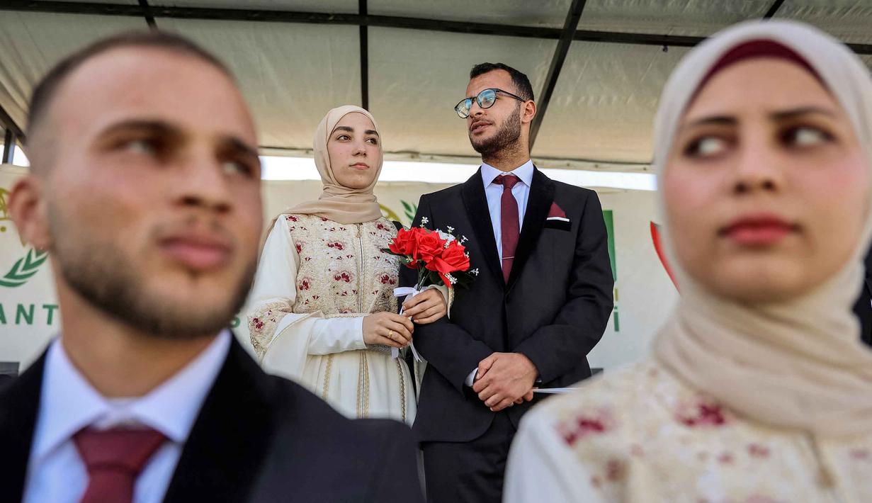 Acara tersebut diselenggarakan oleh Turkish Humanitarian Relief Foundation (IHH) sebagai bentuk dukungan bagi pasangan yatim piatu di tengah situasi sulit yang masih melanda Gaza. Tampak dalam foto, para pengantin Palestina berkumpul selama perayaan pernikahan massal untuk para pengantin Palestina yang diselenggarakan oleh Yayasan Bantuan Kemanusiaan Turki (IHH) di Kota Gaza pada 11 Mei 2026. (Omar AL-QATTAA/AFP)