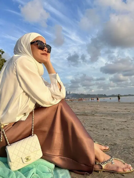 Bermain di pantai, Olla tampil tertutup mengenakan kemeja putih panjang serasi dengan pashmina plisket. Dipadukan bawahan coklat dan tas serta sandal Chanel. [Instagram/@ollaramlan]