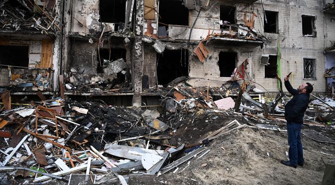 Seorang pria mengambil gambar sebuah bangunan tempat tinggal yang rusak setelah peluru militer Rusia menghantam di Koshytsa Street, Kiev, Ukraina (25/2/2022). Pasukan Rusia mencapai pinggiran Keiv pada hari Jumat (24/2). (AFP/Daniel Leal)