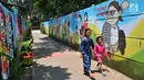 Dua anak melintas di 'Gang Mural', Kelurahan Rorotan, Jakarta, Kamis (29/3). Ide Gang Mural ini diinisiasi oleh Kelurahan Rorotan dan gambar-gambar di sepanjang tembok dilukis oleh petugas PPSU. (Merdeka.com/Iqbal S Nugroho)