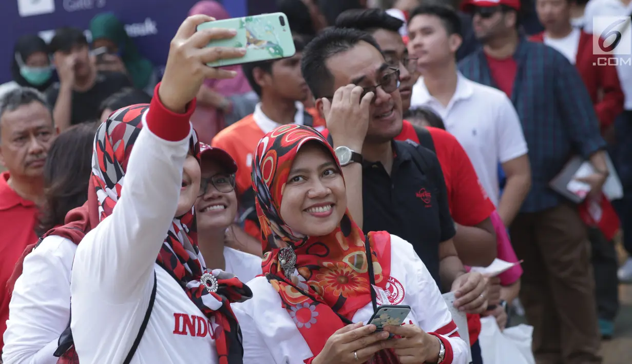 Calon penonton seremoni pembukaan Asian Games 2018 berswafoto jelang masuk kawasan GBK, Jakarta, Sabtu (18/8). Asian Games 2018 akan berlangsung hingga 2 September, mendatang. (Liputan6.com/Helmi Fithriansyah)