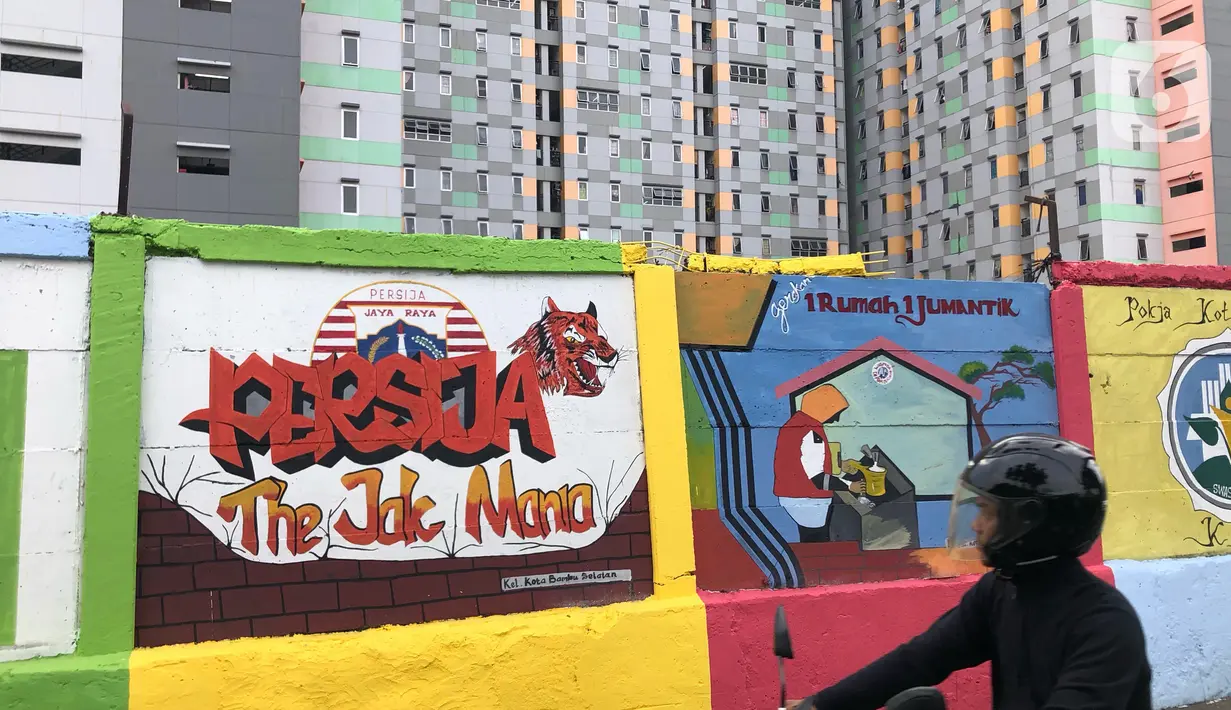 Pengendara motor mengamati mural bertema Kota Jakarta di sekitar Rusunawa KS Tubun, Jakarta, Senin (23/11/2020). Mural tersebut dibuat guna memercantik lingkungan di sekitar rusun agar lebih berwarna dan tidak tampak kumuh. (Liputan6.com/Immanuel Antonius)