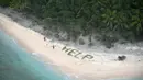 Dua orang berdiri disamping tulisan "Help" yang tersusun dari dahan pohon palem di pulau tak berpenghuni Faradik, Mikronesia, 7 April 2016. Tiga orang pelaut berhasil diselamatkan pasukan AL Amerika Serikat setelah tiga hari terdampar. (AFP Photo)