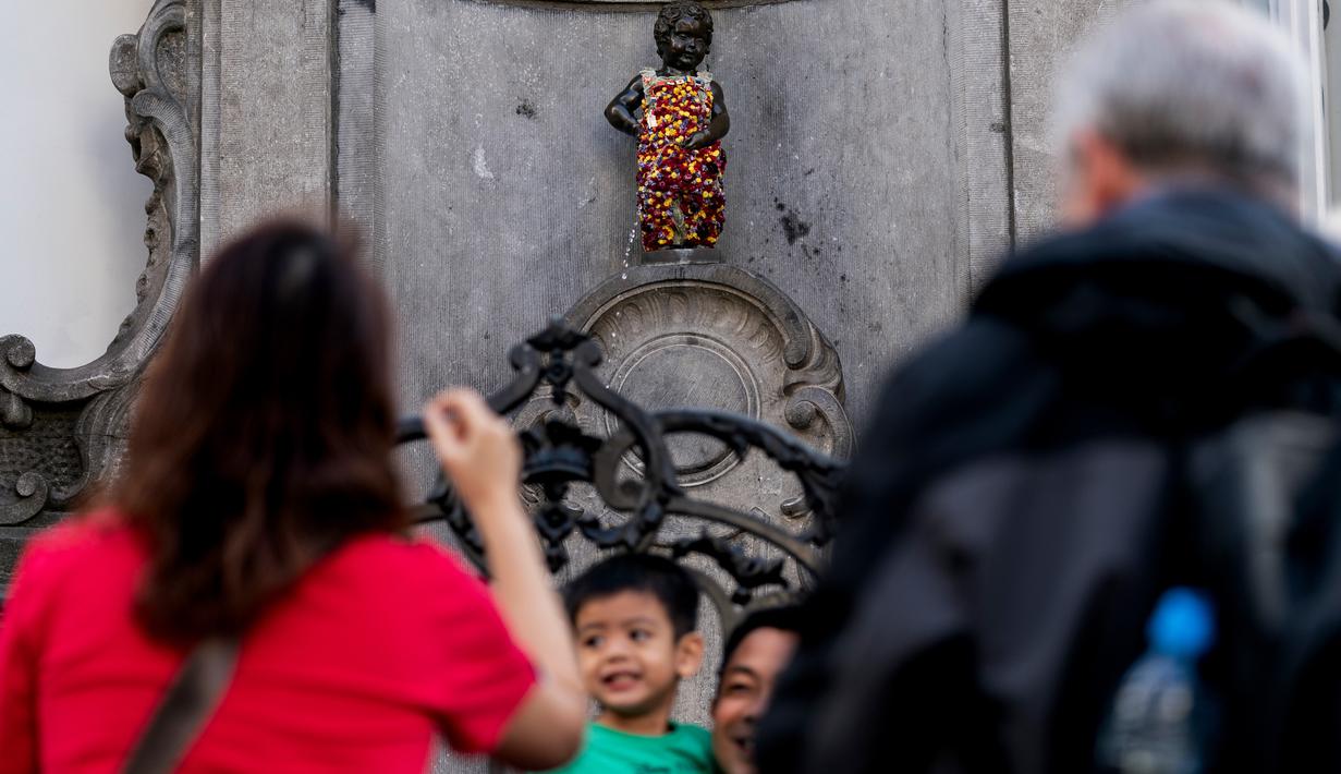 Wisatawan berfoto dekat patung 'Manneken Pis' dalam balutan baju bermotif bunga di ibu kota Belgia, Brussels, Senin (12/8/2019). Patung anak laki-laki yang sedang buang air kecil ini menjadi salah satu daya tarik uta di kota cantik tersebut. (Photo by Kenzo TRIBOUILLARD / AFP)