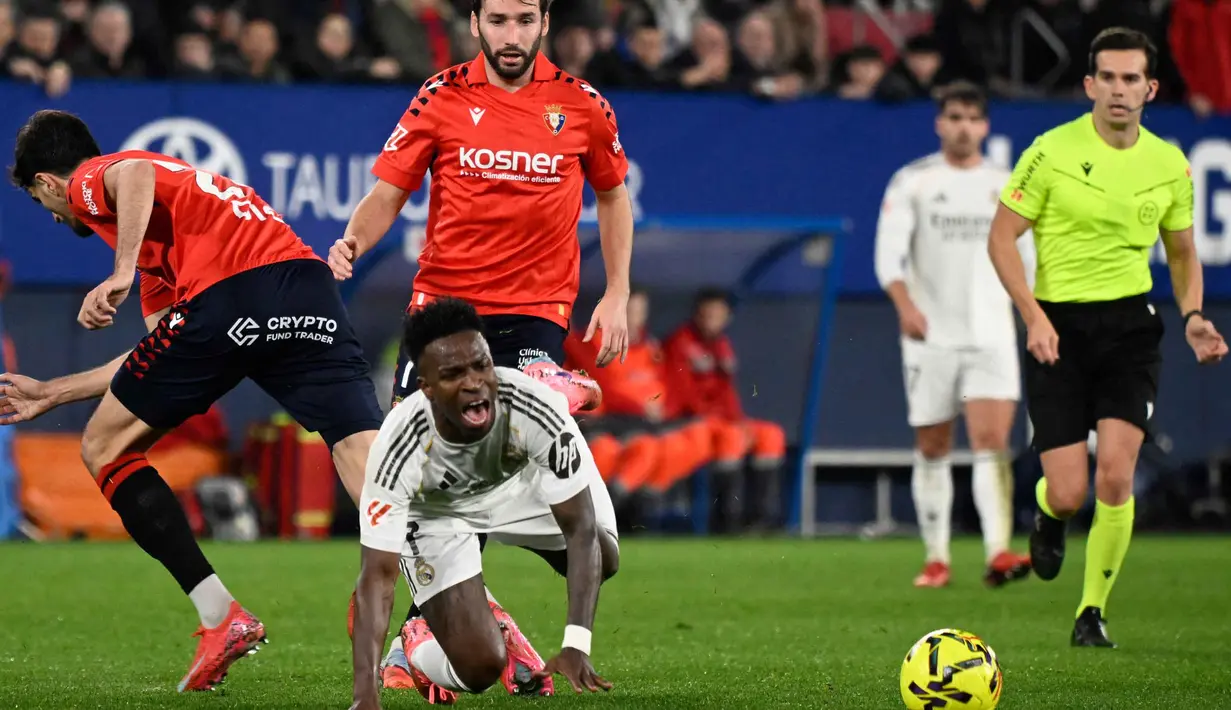 Keunggulan 1-0 untuk tuan rumah bertahan hingga waktu turun minum. Tampak dalam foto, penyerang Real Madrid asal Brasil, Vinicius Junior terjatuh saat berebut bola dengan bek Osasuna asal Spanyol, Alejandro Catena (kiri) selama pertandingan pekan ke-25 La Liga 2025/2026 di Stadion El Sadar, Pamplona pada Sabtu 21 Februari 2026 waktu setempat atau Minggu (22/2/2026) dini hari WIB. (ANDER GILLENEA/AFP)