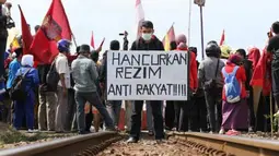 Seorang demonstran membawa poster di tengah rel kereta api saat melakukan aksi memblokir jalur KA di Pintu perlintasan KA Stasiun Purwokerto, Banyumas, Jateng, Jumat (30/3). Mereka menolak rencana kenaikan BBM yang akan dilakukan pemerintah dengan cara memblokir jalur KA tersebut. (Antara)