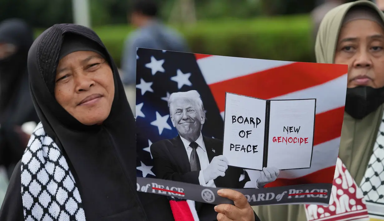 Sebelumnya, Indonesia menyatakan akan bergabung dalam Board of Peace (BOP), sebuah dewan perdamaian yang diinisiasi oleh Amerika Serikat. Pihak Kementerian Luar Negeri menegaskan bahwa keterlibatan Indonesia bertujuan membuka jalur logistik bantuan ke Gaza dan mendorong kemerdekaan Palestina dari dalam forum internasional. Tampak dalam foto, seorang aktivis Muslim memegang poster bergambar Presiden Donald Trump saat unjuk rasa mendukung warga Palestina di Gaza, di depan Kedutaan Besar Amerika Serikat, Jakarta, Jumat 13 Februari 2026. (AP Photo/Achmad Ibrahim)