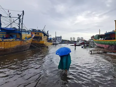 Nelayan melintasi banjir rob saat cuaca ekstrem di Pelabuhan Muara Baru, Penjaringan, Jakarta Utara, Rabu (28/12/2022). Banjir ROB, hujan deras dan  cuaca buruk melanda kawasan Pelabuhan Muara Baru saat siang menjelang sore hari. (Liputan6.com/Johan Tallo)