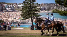 Polisi berkuda berpatroli saat mengunjungi pantai Bondi di Sydney, Australia pada 5 Oktober 2020. Kerumunan warga dan aktivitas yang ramai ini membuat penerapan jarak sosial menjadi nyaris mustahil dilakukan.  (Photo by DAVID GRAY / AFP)