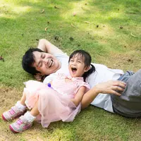 Potret ayah dan anak berbaring dan tertawa bersama dengan penuh kebahagiaan saat bermain di atas hamparan rumput yang hijau. Gemes sekali, ya, melihatnya. (SUKJAI PHOTO/ Shutterstock.com)