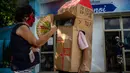 Seorang perempuan berbincang dengan pensiunan perawat bernama Feridia Rojas (82) yang memakai kotak kardus untuk melindungi dirinya dari penyebaran Covid-19 di Havana, Kuba, 8 Juli 2020. Kardus pelindung itu dilengkapi pesan yang ditulis tangan, "I'm home, and you?." (AP/Ramon Espinosa)