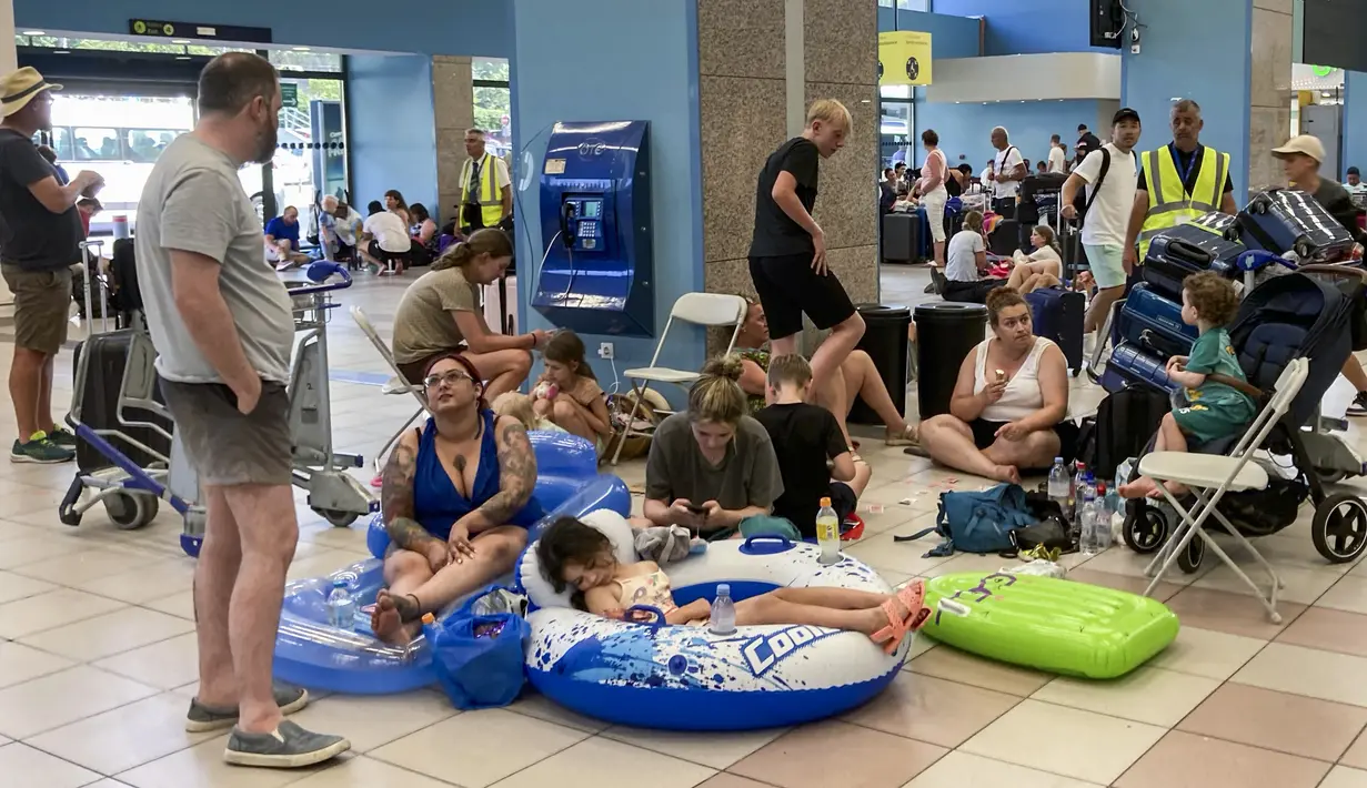 Para turis menunggu di aula keberangkatan bandara saat evakuasi sedang berlangsung akibat kebakaran hutan, di pulau Rhodes, Yunani, Minggu (23/7/2023). (Will VASSILOPOULOS / AFP)
